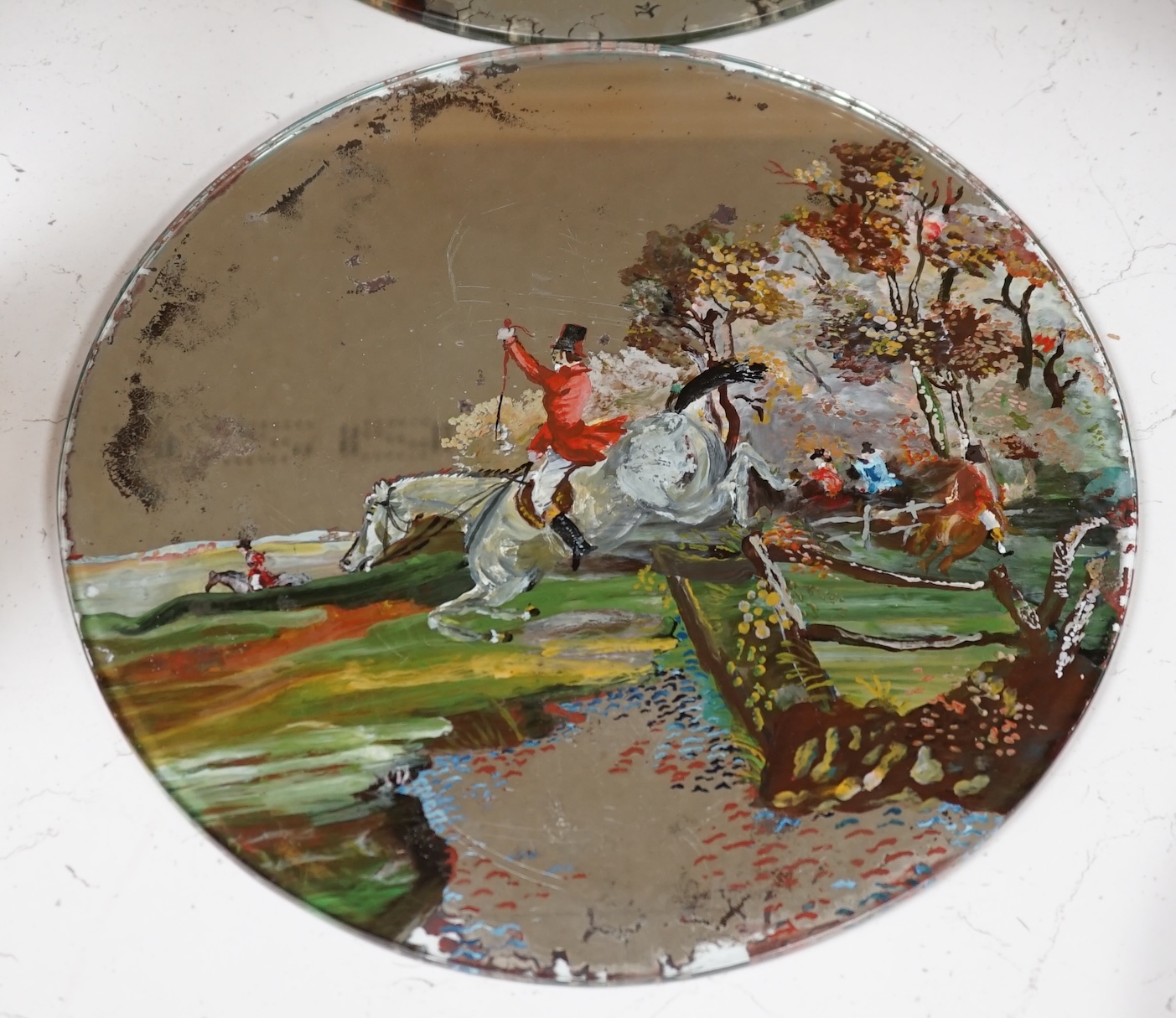 Three reverse painted mirrored glass place mats including a pair depicting landscapes with figures on horseback, largest 30cm diameter. Condition - fair
